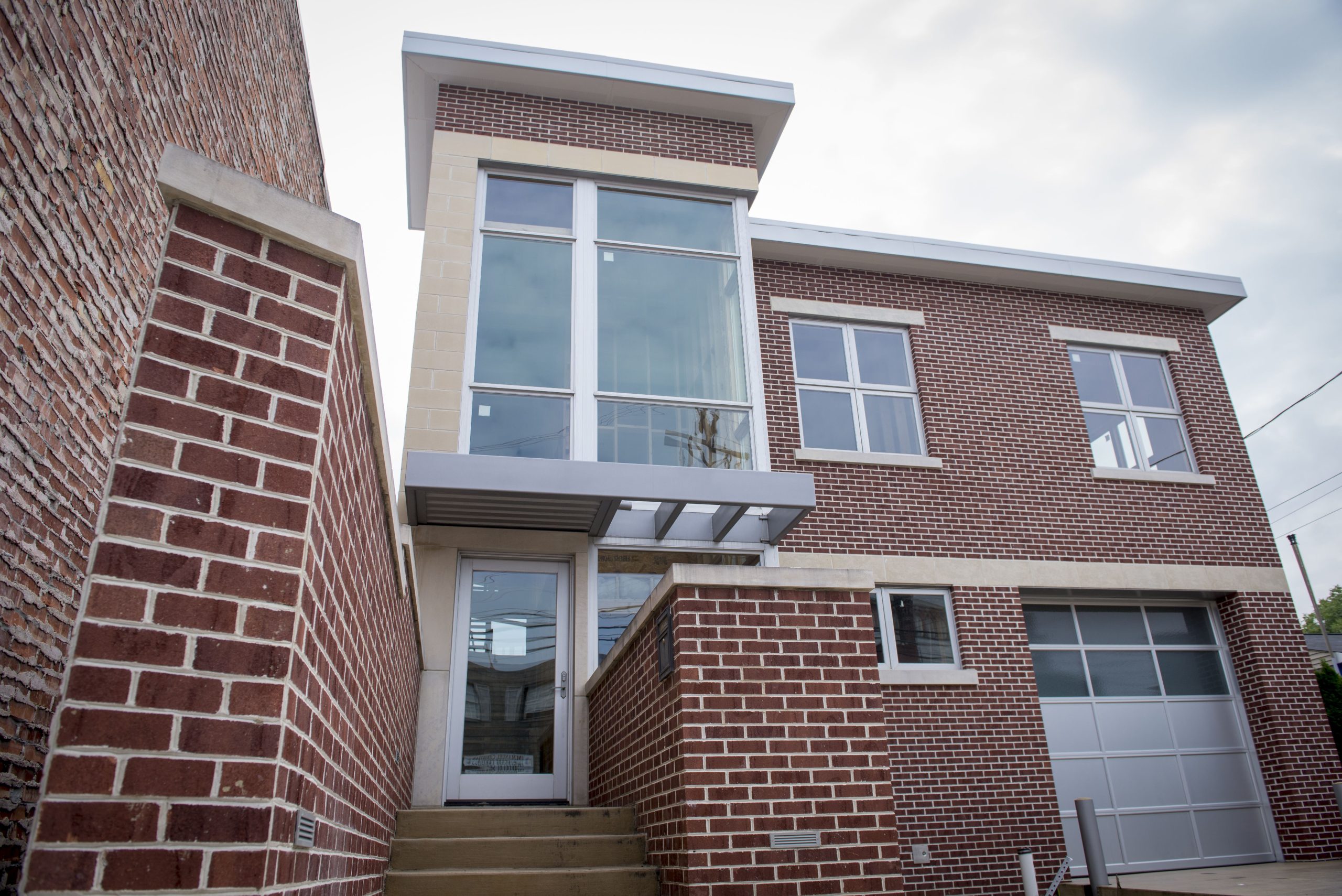 Looking up at the entryway and front door of a home with brick siding, large windows and a modern look