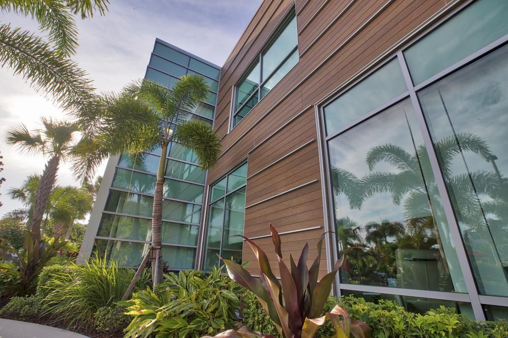 Looking up at a wall of windows next to a wall of VintageWood fiber cement siding from Nichiha surrounded by palm trees and tropical plants.