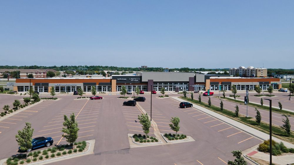 A faraway shot of a strip mall at South Lorraine Place utilizing Nichiha’s fiber cement cladding. A large parking lot with a few cars in front of the strip mall.