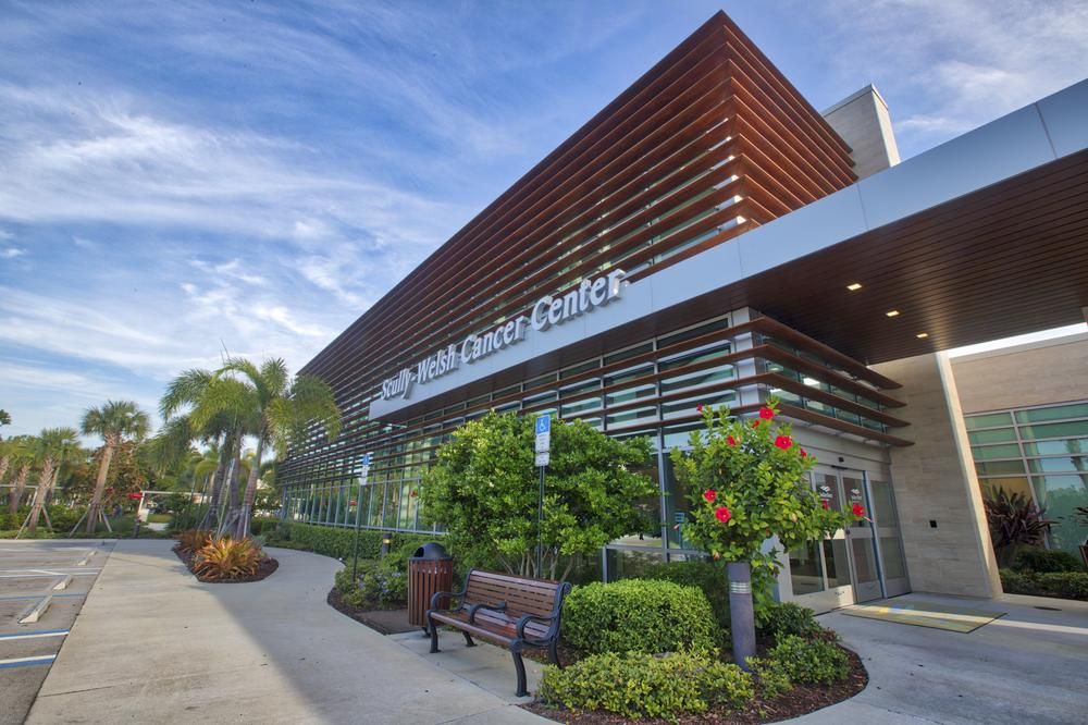 A shot of the Scully Welsh Cancer Center in Florida utilizing Nichiha&rsquo;s VintageWood fiber cement siding in Cedar. There are palm trees around it, a lot of windows on the building and a large telescope sculpture propped in front.
