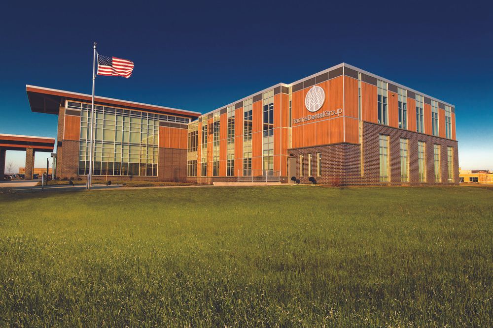 A photo of Racine Dental Group building utilizing Nichiha&rsquo;s VintageWood fiber cement cladding in Cedar with a grass field in front and an American flag blowing in the wind.