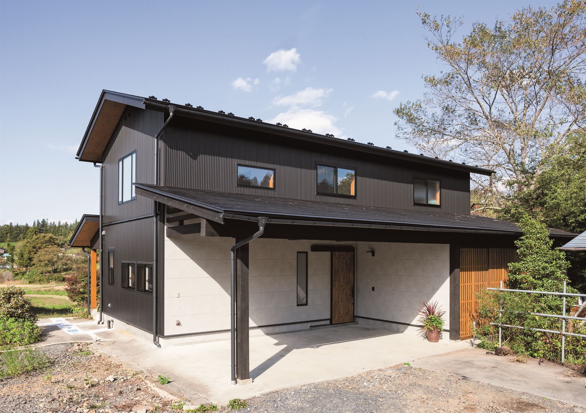A modern home featuring black wood textured vertical siding on the side and second story, a black roof and light grey stone texture siding around the wood door.