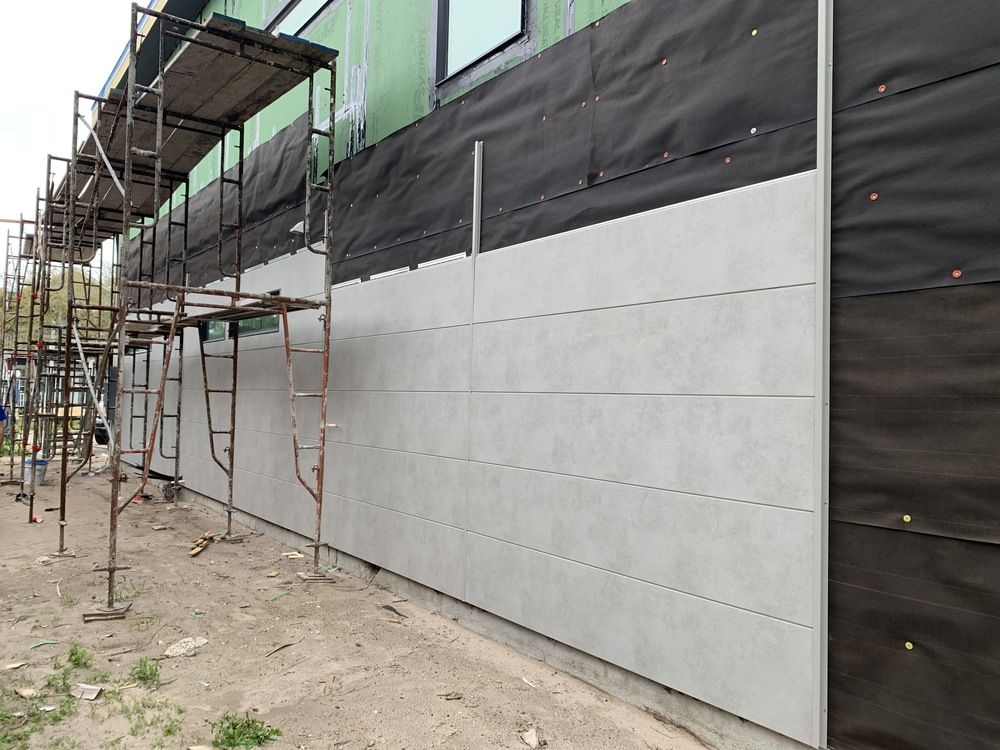 A wall under construction with light gray horizontal siding and a black rainscreen.