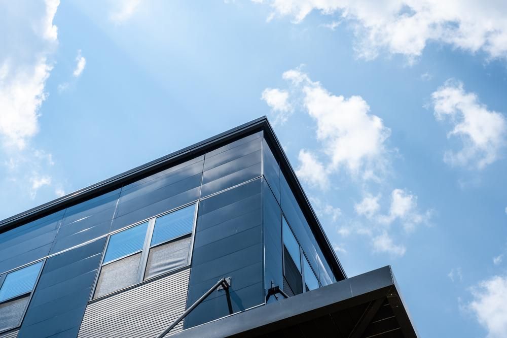 View from the base of a commercial building with black and silver metal exterior and the blue sky and sparse clouds above.