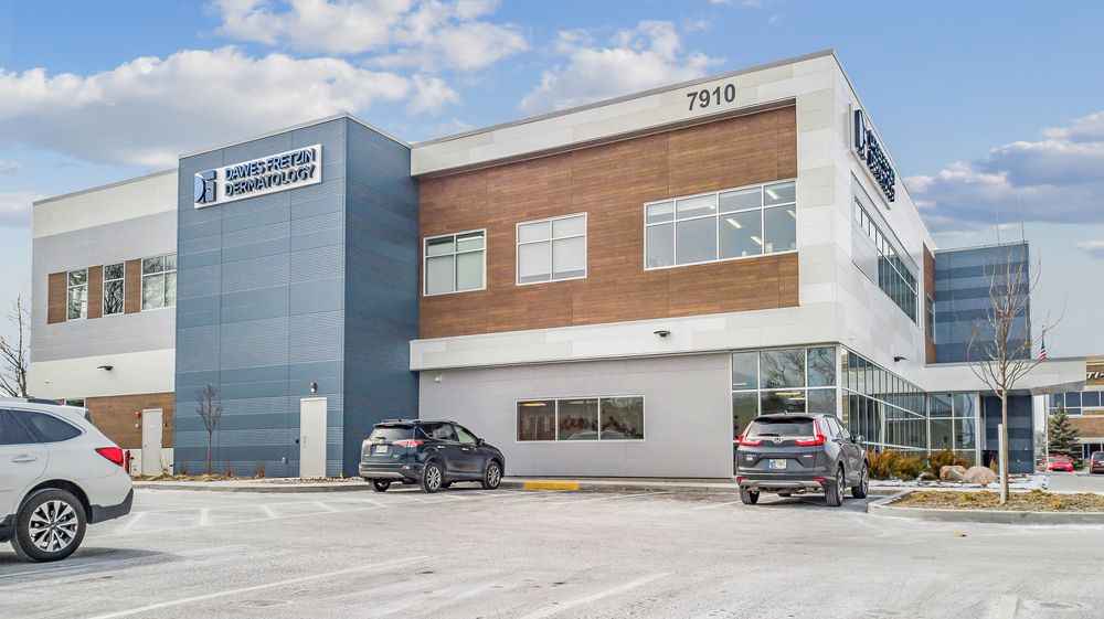 Dermatology office with large parking lot that has cars and blue sky with clouds