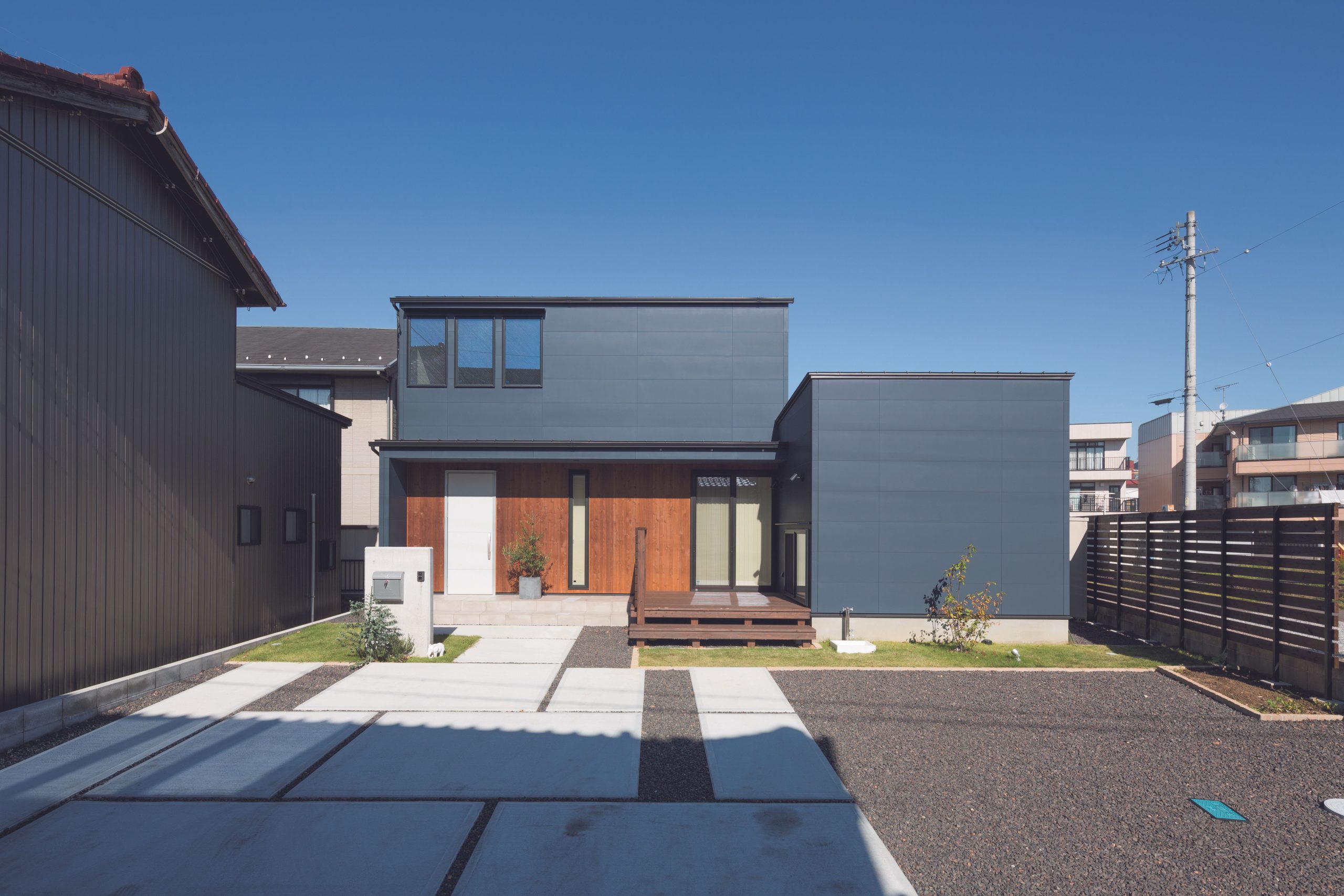 Front-facing view of a home with navy and wooden siding and a concrete-tiled and gravel driveway