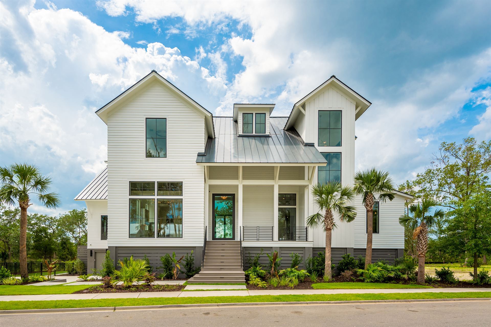 A front street view of a white wood fiber cement sided house with a black roof, black railing and black-framed windows, surrounded by palm trees.