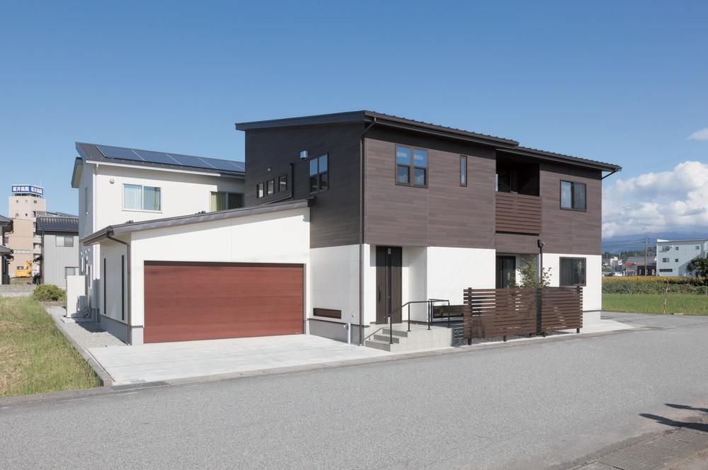 Nichiha&rsquo;s fiber cement siding in white and dark brown on a home with a blue sky in the background and a large brownish-red garage door.