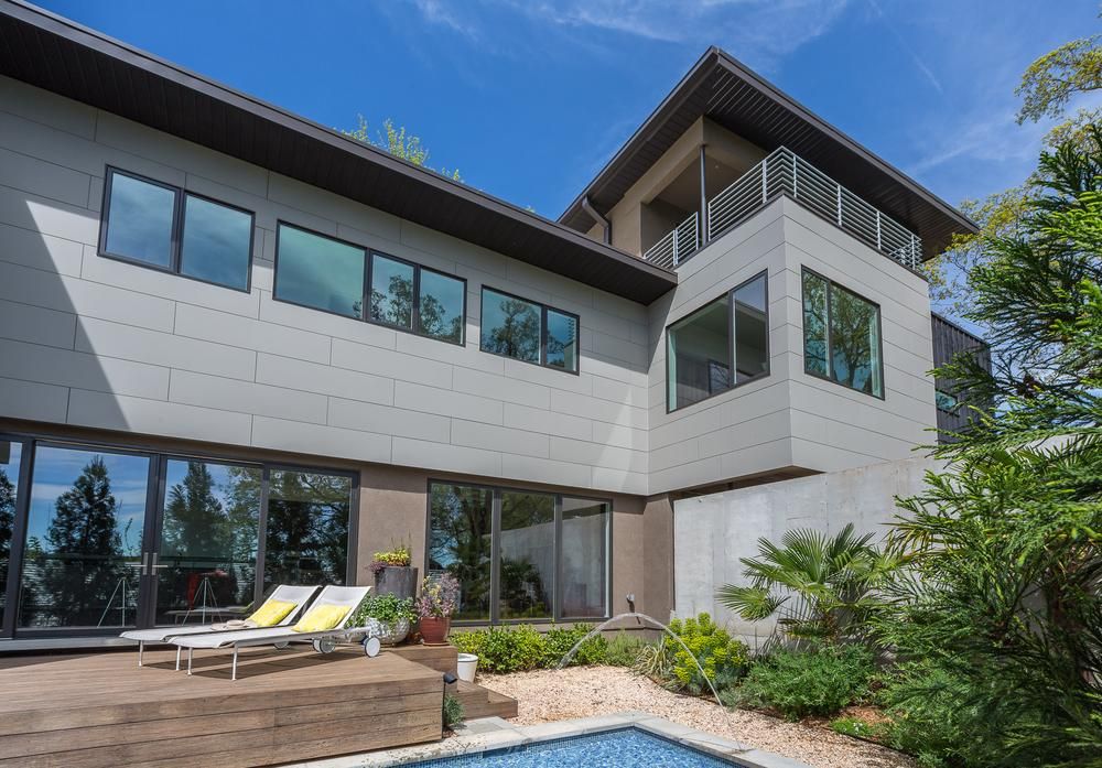 This modern home with Nichiha&rsquo;s fiber-cement siding has a pool in the backyard with two pool chairs. 