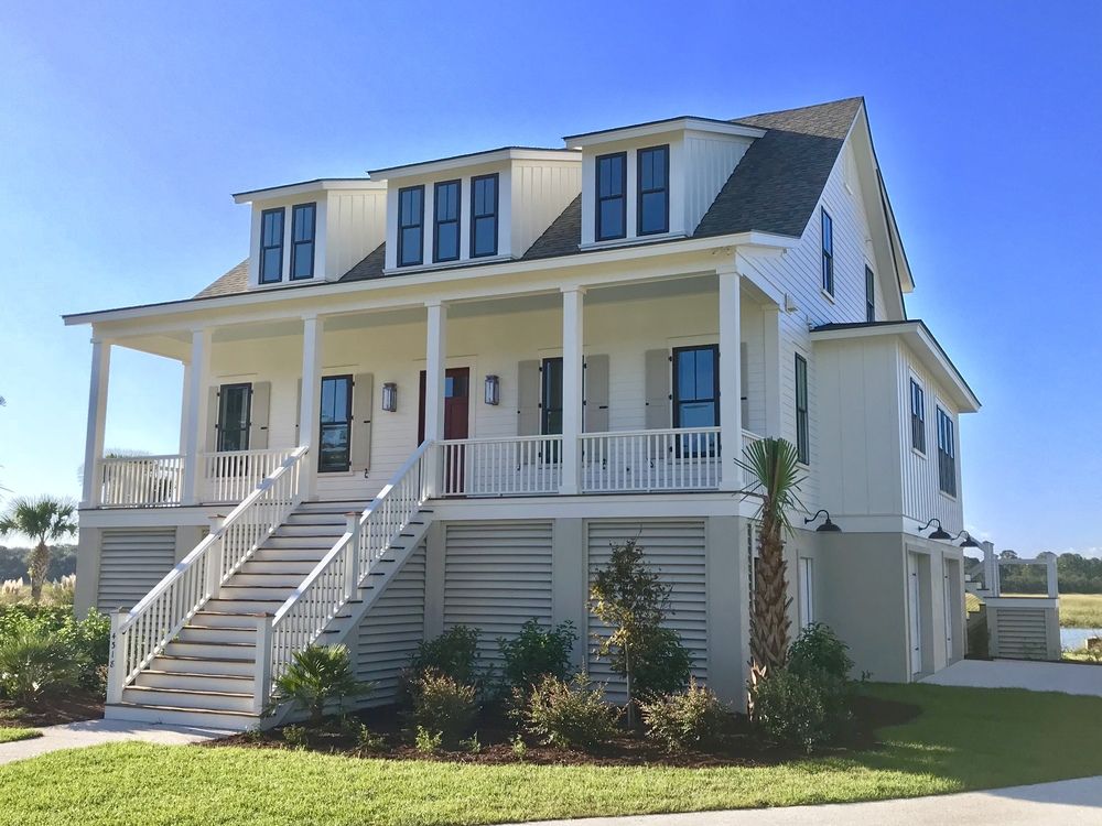 This white beach house with a front porch and palm trees overlooks a creek with marsh grass.