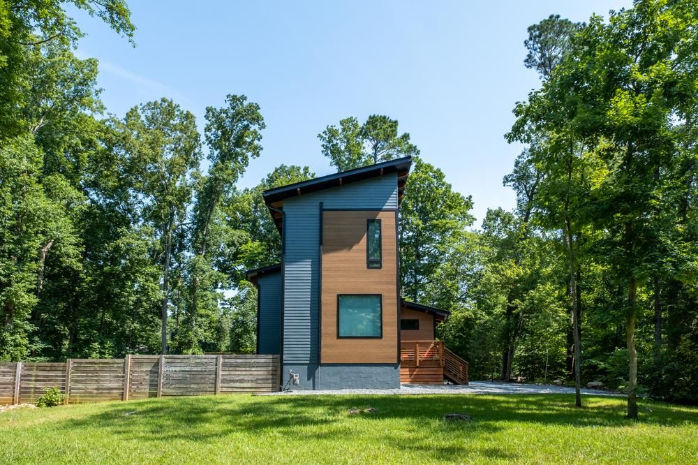 A side view of a two-story home with blue and wood-like siding. There are trees surrounding the property.