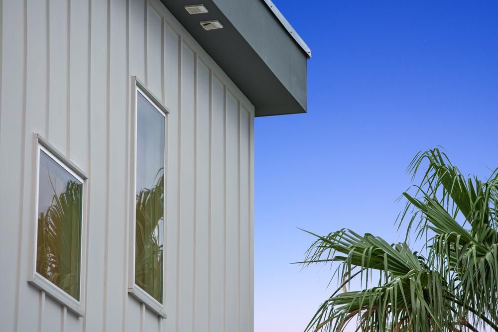 Close-up of home with gray siding against blue sky and palm tree.