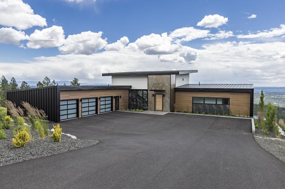 A brown, black, white, and stone accented home protected with Nichiha&rsquo;s fiber cement siding sits atop a hill with a large driveway and blue, cloudy skies in the background.
