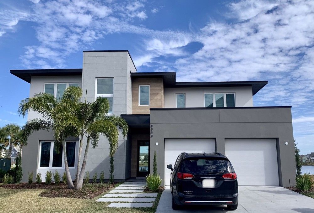Square-roofed home with dark and light gray siding with palm trees in the yard.