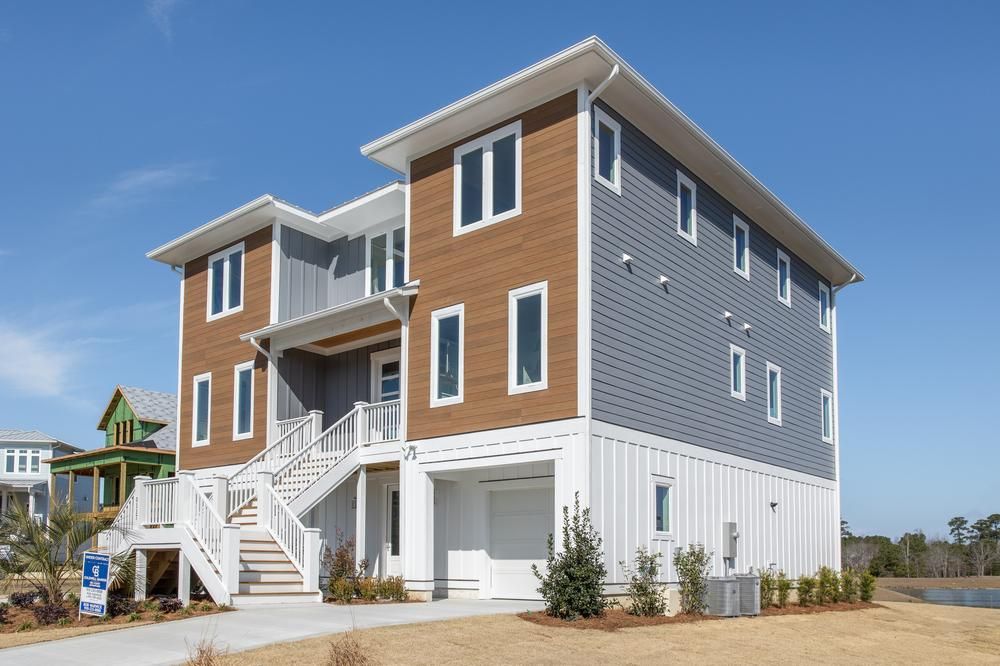 Three-story beach home with wood look and gray fiber cement siding with white staircase leading to porch and front door.