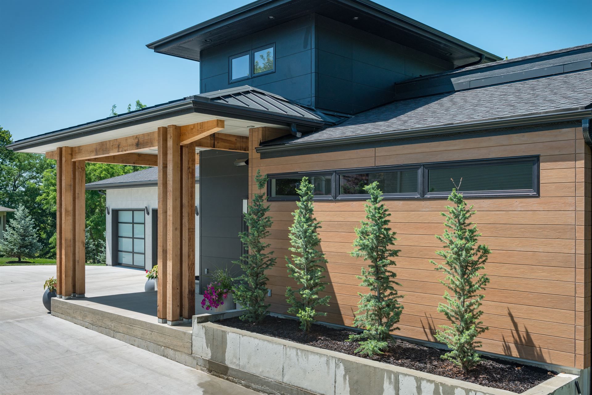 A side view of a modern home featuring Nichiha VintageWood siding behind a cement planter filled with four small evergreen trees.