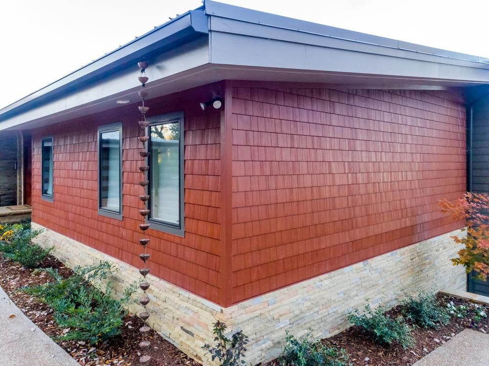 A faux cedar shake sided home with a stacked stone base, black windows and a rain chain.