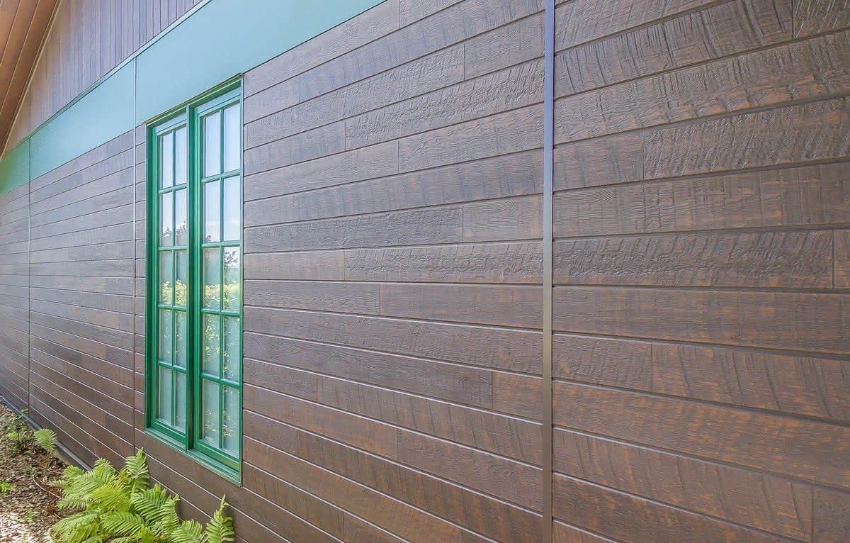 Brown horizontal wood-look siding around a green-trimmed window.
