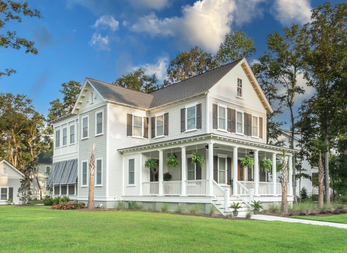 White two-story farmhouse with a wraparound porch and lawn.