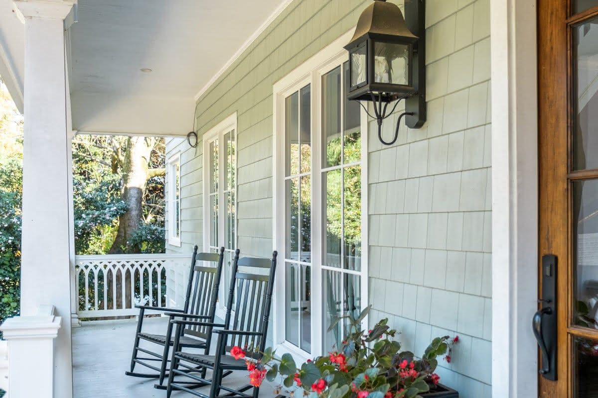 Covered porch with white shake siding and two black rocking chairs.