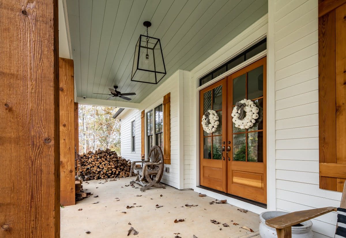 Covered front porch with wood posts, glazed wood doors, and planters.